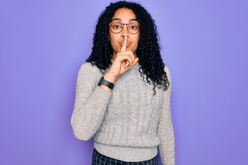 Young african american woman wearing casual sweater and glasses over purple background asking to be quiet with finger on lips. Silence and secret concept.