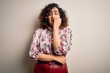 Young beautiful curly arab woman wearing floral t-shirt standing over isolated white background looking stressed and nervous with hands on mouth biting nails. Anxiety problem.
