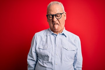 Obraz premium Middle age handsome hoary man wearing casual striped shirt and glasses over red background sticking tongue out happy with funny expression. Emotion concept.