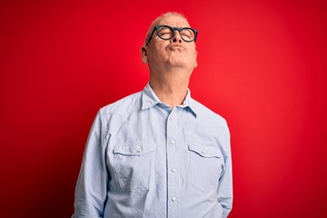 Middle age handsome hoary man wearing casual striped shirt and glasses over red background looking at the camera blowing a kiss on air being lovely and sexy. Love expression.