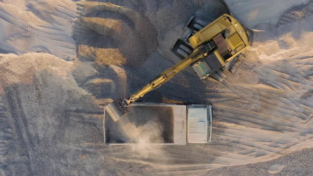 Aerial top down view of excavator loading sand into a truck body