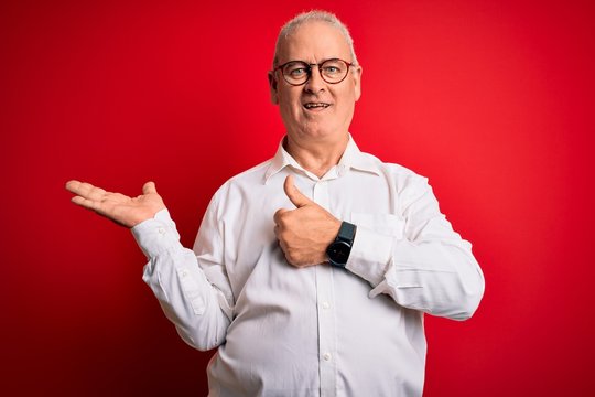 Middle age handsome hoary man wearing casual shirt and glasses over red background Showing palm hand and doing ok gesture with thumbs up, smiling happy and cheerful
