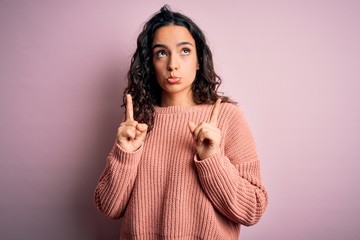 Young beautiful woman with curly hair wearing casual sweater over isolated pink background Pointing...