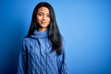 Young beautiful chinese woman wearing casual sweater over isolated blue background with a happy and...
