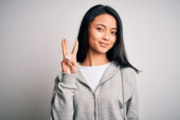 Young beautiful chinese sporty woman wearing sweatshirt over isolated white background showing and pointing up with fingers number three while smiling confident and happy.