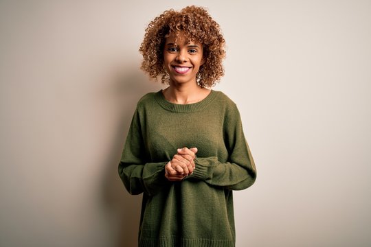 Beautiful african american woman with curly hair wearing casual sweater over white background with hands together and crossed fingers smiling relaxed and cheerful. Success and optimistic