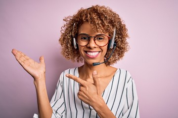 African american curly call center agent woman working using headset over pink background amazed...