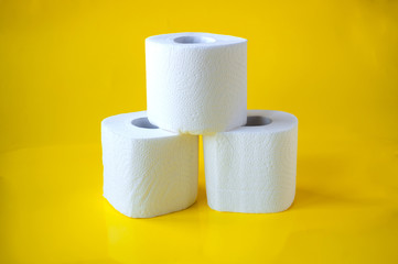 Three rolls of white toilet paper on a yellow background