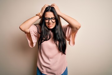 Young brunette elegant woman wearing glasses over isolated background suffering from headache desperate and stressed because pain and migraine. Hands on head.