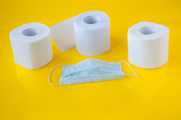 Three rolls of white toilet paper and a medical mask on a yellow background