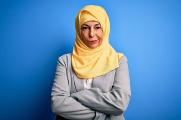 Middle age brunette business woman wearing muslim traditional hijab over blue background skeptic and nervous, disapproving expression on face with crossed arms. Negative person.