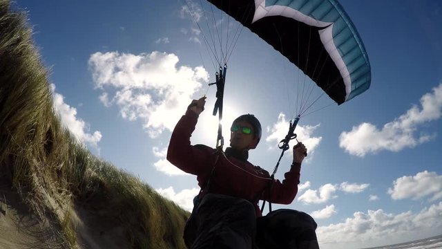 Paraglider pilot soaring above a sandy beach with the sun in backlight. Coastal flight, wind lift, and freedom concept.
