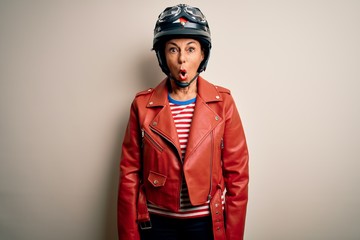 Middle age motorcyclist woman wearing motorcycle helmet and jacket over white background afraid and shocked with surprise expression, fear and excited face.