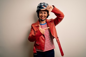Middle age motorcyclist woman wearing motorcycle helmet and jacket over white background smiling making frame with hands and fingers with happy face. Creativity and photography concept.