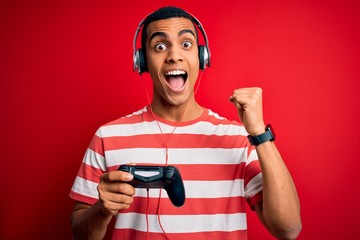 Handsome african american gamer man playing video game using jostick and headphones screaming proud and celebrating victory and success very excited, cheering emotion © Krakenimages.com
