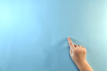 Naklejka premium Children's right hand with the index finger down and pointing to a blue surface on a backlit background on the right.