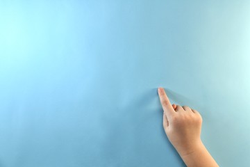 Children's right hand with the index finger down and pointing to a blue surface on a backlit background on the right.