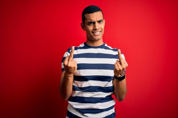 Handsome african american man wearing casual striped t-shirt standing over red background Showing...