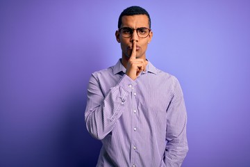 Obraz premium Handsome african american man wearing striped shirt and glasses over purple background asking to be quiet with finger on lips. Silence and secret concept.