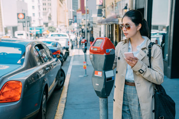 Obraz premium Young charming asian Japanese woman paying for car parking at machine with mobile phone online app. beautiful office lady local lifestyle in san francisco usa. female holding cellphone doing payment