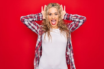 Young beautiful blonde woman wearing casual shirt standing over isolated red background Smiling cheerful playing peek a boo with hands showing face. Surprised and exited