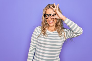 Beautiful blonde woman wearing casual striped t-shirt and glasses over purple background doing ok gesture with hand smiling, eye looking through fingers with happy face.