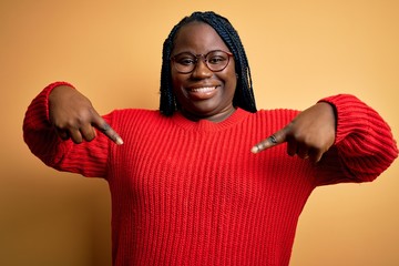 African american plus size woman with braids wearing casual sweater over yellow background looking...