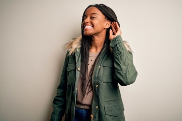 Young african american woman wearing winter parka coat over isolated background smiling with hand over ear listening an hearing to rumor or gossip. Deafness concept. © Krakenimages.com