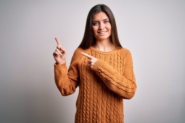 Young beautiful woman with blue eyes wearing casual sweater standing over white background smiling and looking at the camera pointing with two hands and fingers to the side.