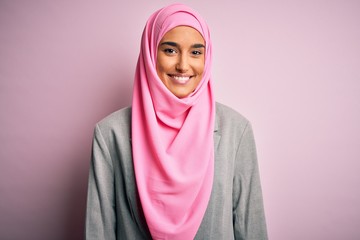 Young beautiful brunette businesswoman wearing pink muslim hijab and business jacket with a happy and cool smile on face. Lucky person.
