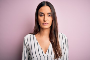 Young beautiful brunette woman wearing casual striped shirt over isolated pink background with...