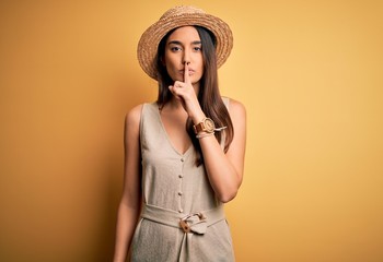 Young beautiful brunette woman on vacation wearing casual dress and hat asking to be quiet with finger on lips. Silence and secret concept.