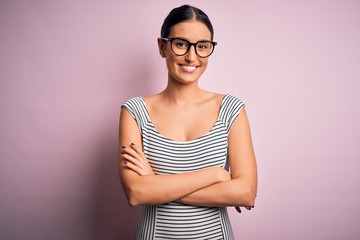 Young beautiful woman wearing casual striped dress and glasses over pink background happy face...
