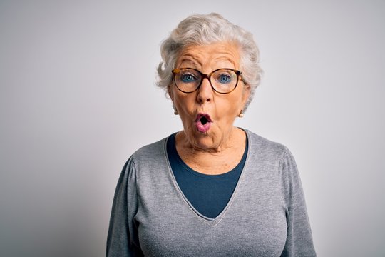 Senior beautiful grey-haired woman wearing casual sweater and glasses over white background afraid and shocked with surprise expression, fear and excited face.