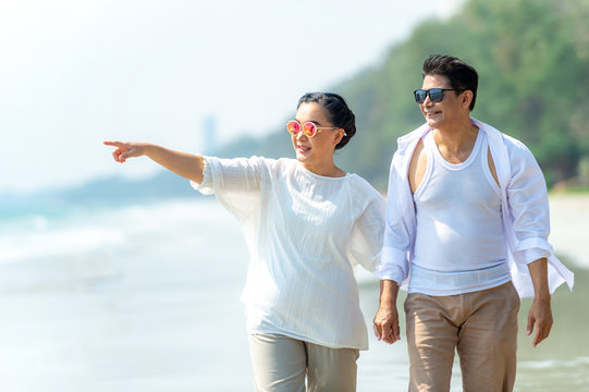 Happy Asian senior couple family holding hands together and walking on the beach with smiling. Healthy retirement old age people man and woman enjoying and relaxing romance summer holiday vacation