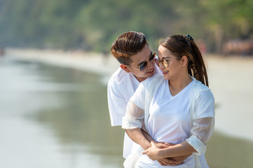 Fototapeta premium Happy young Asian couple man hugging beautiful woman on tropical beach and looking at each other with smiling face. Healthy family people enjoying relax lifestyle in romantic summer holiday vacation.