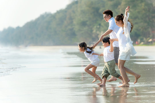 Smiling Young Asian Happy Family Parents With Child Running And Having Fun Together On The Beach In Summertime. Father, Mother And Kids Relax And Enjoy Summer Lifestyle Travel Holiday Vacation.