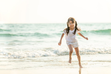 Fototapeta na wymiar Portrait Happy cute little Asian girl running and playing with smiling and laughing on tropical beach at sunset. Portrait of Adorable young child kids having fun in summer holiday vacation travel.