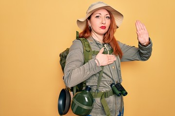 Young redhead backpacker woman hiking wearing backpack and hat over yellow background Swearing with...