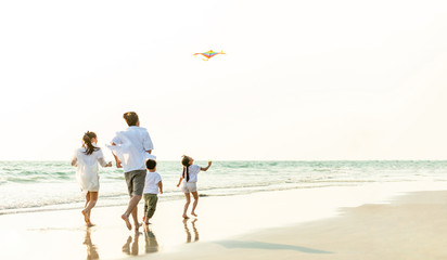 Happy Young Asian family parents with child running and having fun with playing kite together on the beach in summertime. Father, mother and kids relax and enjoy summer lifestyle travel vacation