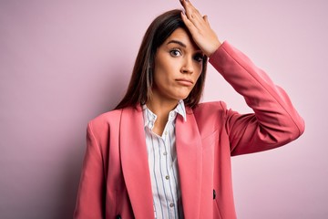 Young beautiful brunette woman wearing jacket standing over isolated pink background surprised with...