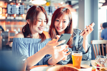 cheerful young friends looking at smart phone in restaurant