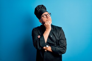 Middle age handsome grey-haired chef man wearing cooker uniform and hat with hand on chin thinking about question, pensive expression. Smiling with thoughtful face. Doubt concept.