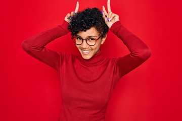 Fototapeta na wymiar Young beautiful african american afro woman wearing turtleneck sweater and glasses Posing funny and crazy with fingers on head as bunny ears, smiling cheerful