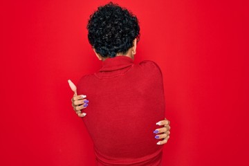 Young beautiful african american afro woman wearing turtleneck sweater and glasses Hugging oneself...