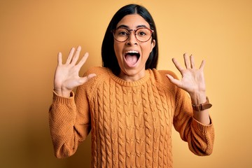 Young beautiful hispanic woman wearing glasses over yellow isolated background celebrating crazy and amazed for success with arms raised and open eyes screaming excited. Winner concept