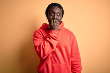 Obraz premium Young african american sporty man wearing sweatshirt with hoodie over yellow background looking stressed and nervous with hands on mouth biting nails. Anxiety problem.