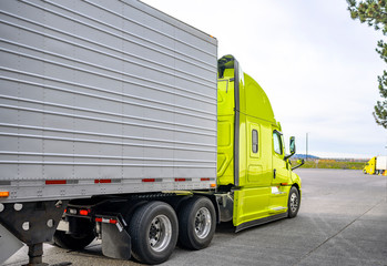 Bright green bonnet big rig semi truck transporting cargo in refrigerator semi trailer running out...