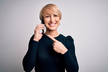 Young blonde woman with short hair having a conversation talking on smartphone very happy pointing with hand and finger