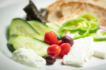 Shallow focus view of simple Greek meze food platter; with vegetables, pita, feta, and grape leaves